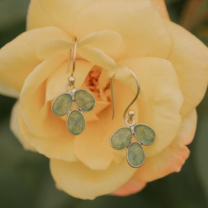 May include: A pair of silver dangle earrings with light blue and green glass teardrop-shaped charms. The earrings are hanging from a yellow rose.