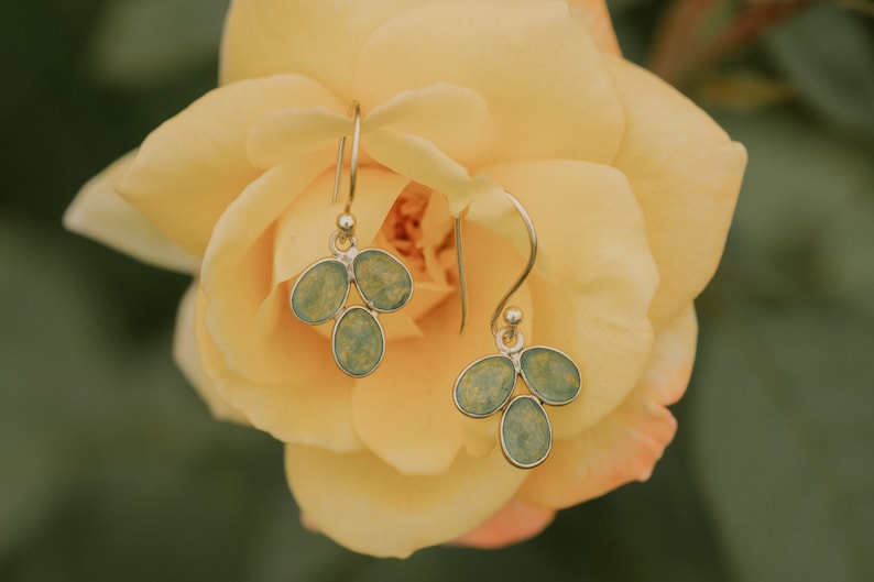 May include: A pair of silver dangle earrings with light blue and green glass teardrop-shaped charms. The earrings are hanging from a yellow rose.