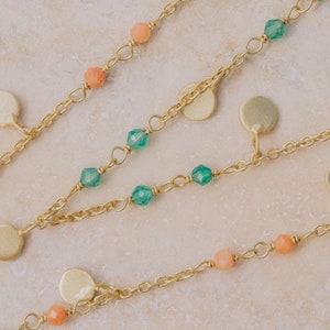 May include: A gold chain necklace with green and peach colored beads and gold disc charms.