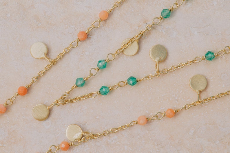 May include: A gold chain necklace with green and peach colored beads and gold disc charms.
