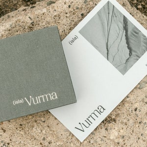 May include: A gray box with the text "(isla) Vurma" printed in white. A white card with a black and white photo of a landscape and the text "(isla) Vurma" and "islayvurma.com" printed in black.