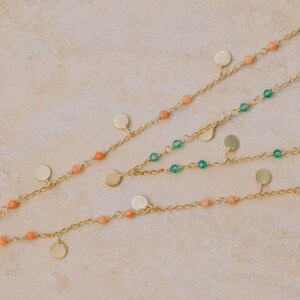 May include: Three gold chains with small round pendants and beads. The top chain has green beads, the middle chain has peach beads, and the bottom chain has peach beads.