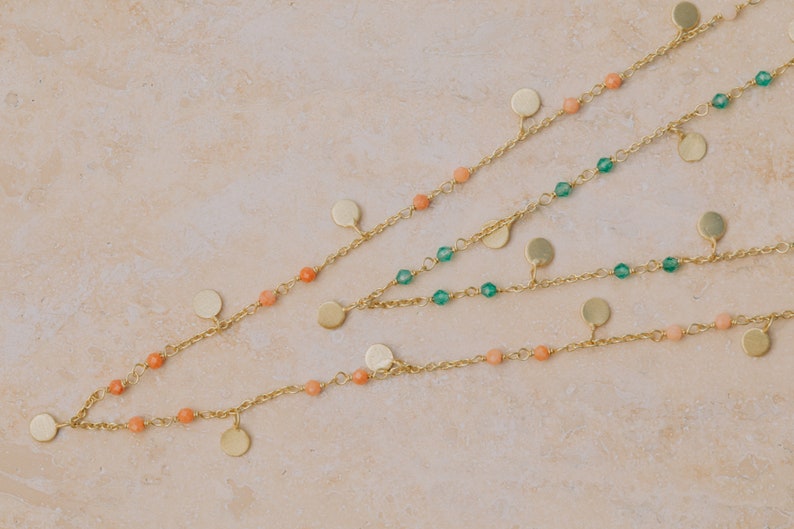 May include: Three gold chains with small round pendants and beads. The top chain has green beads, the middle chain has peach beads, and the bottom chain has peach beads.