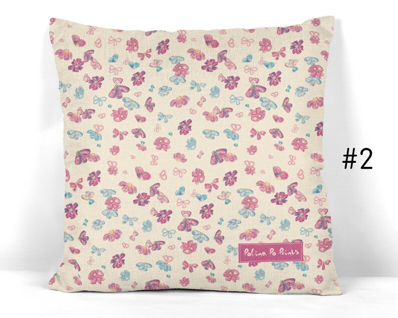 May include: A cream-colored pillow with a pink and blue butterfly and flower pattern. The pillow has the text "Polina Po Prints" in pink.