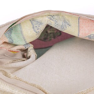 May include: A beige zippered pouch with a colorful striped lining. The lining has a pattern of small squares and a floral design.