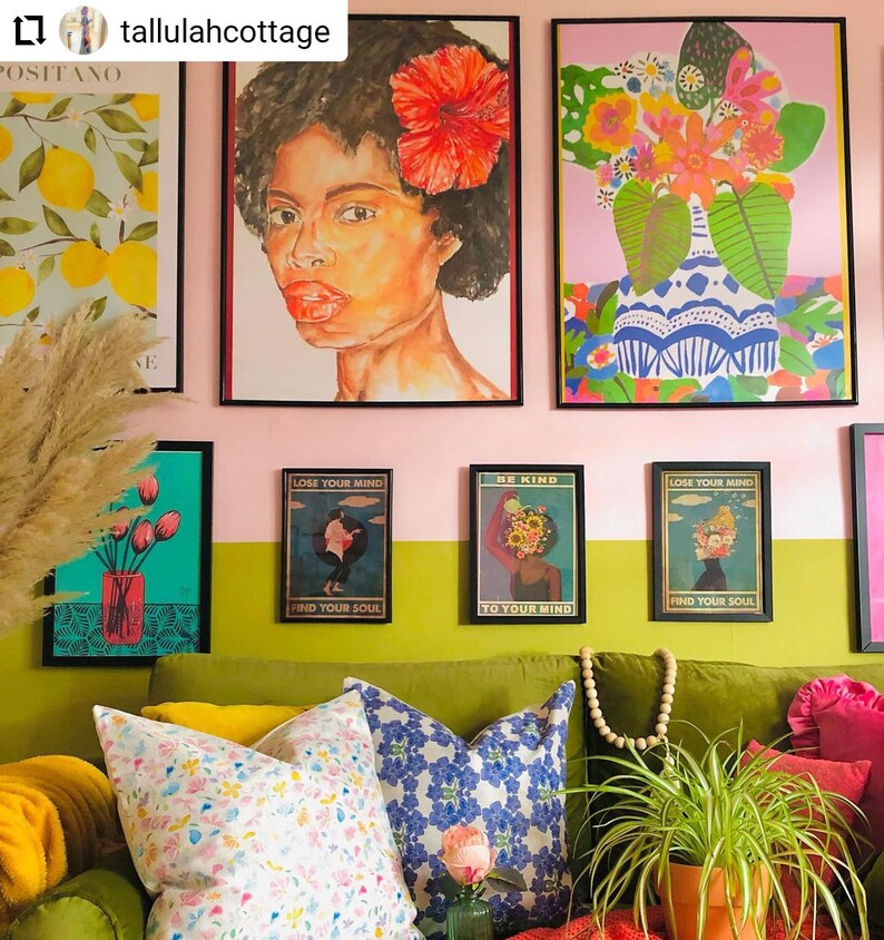 May include: A green velvet sofa with yellow, blue, and white patterned pillows. The sofa is in front of a wall with a pink and green color scheme. There are several framed prints on the wall, including a portrait of a woman with a red flower in her hair, a floral print, and three prints with the text "Lose Your Mind, Find Your Soul" and "Be Kind, To Your Mind".