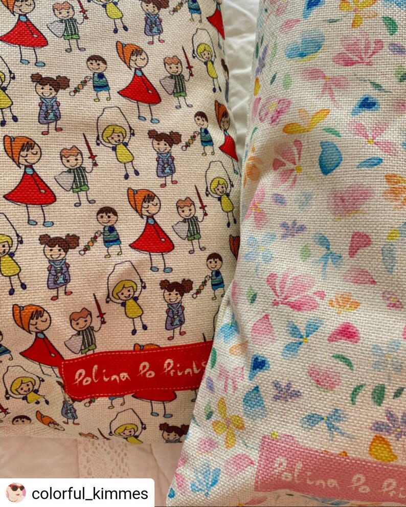 May include: Two white pillow covers with different patterns. One cover features a repeating pattern of colorful stick figures playing with toys. The other cover features a repeating pattern of colorful flowers and butterflies. Both covers have a red label that says "Polina Po Prints".
