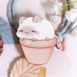 May include: A white cat with pink cheeks sits in a light brown flower pot. The cat is looking to the right and has its paws on the edge of the pot. The pot is on a white background with a light blue hair tie and white flowers.