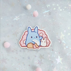 May include: A blue and white cartoon character with large ears and a small white bunny character. The characters are on a pink background with white flowers.