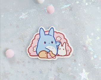 Puede incluir: Un personaje de dibujos animados azul y blanco con orejas grandes y un pequeño conejito blanco. Los personajes están sobre un fondo rosa con flores blancas.