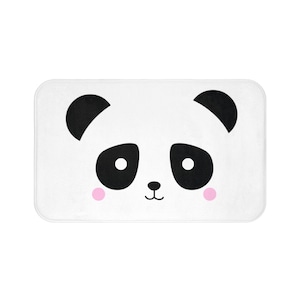 May include: White bath mat with a black and white panda face design. The panda has pink cheeks.