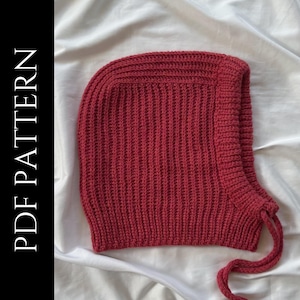 Pode incluir: Um chapéu de crochê vermelho com capuz e cordão de ajuste. O chapéu é feito com ponto canelado.