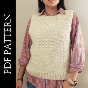 Può includere: Un gilet di uncinetto bianco con un motivo testurizzato. Il gilet è indossato sopra una camicia a righe rosa e bianche.