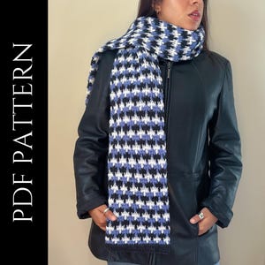 May include: A blue, white, and black crocheted scarf with a houndstooth pattern. The scarf is worn by a person wearing a black leather jacket.