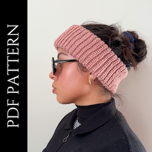 May include: A pink crocheted headband with a ribbed texture. The headband is worn by a person with dark hair and is styled in a bun.