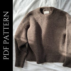 Puede incluir: Un suéter marrón texturizado con cuello redondo y puños y dobladillo acanalados. La imagen incluye el texto "PDF PATTERN" en blanco sobre un fondo negro. El suéter tiene una etiqueta que dice "COSMAUDE".