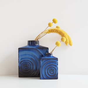 Könnte beinhalten: Zwei blaue Keramikvasen mit einem wirbelnden Muster, die größere Vase enthält einen Strauß getrockneter gelber Blumen.