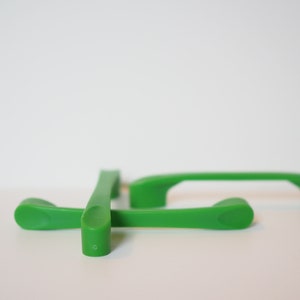 Peut inclure: Trois poignées de porte de placard en plastique vert. Les poignées sont en forme de rectangle arrondi avec une légère courbe en haut.