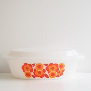 Op de afbeelding: Witte ovale ovenschaal met een bloemenmotief in oranje en rood. De bloemen zijn gestileerd en hebben een retro-look.