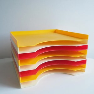 Könnte beinhalten: Ein Stapel aus fünf gelben und roten Kunststoffschalen mit abgerundeten Kanten. Die Schalen sind zum Aufbewahren von Papieren oder Dokumenten gedacht.
