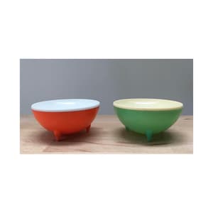 May include: Two small, round bowls with three legs each. The bowl on the left is orange with a white interior. The bowl on the right is green with a cream interior.