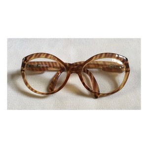 May include: Brown and gold-toned plastic framed glasses with a tortoise shell pattern. The glasses have a large, rounded shape and the brand name "PLAYBOY" is printed on the left frame.