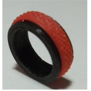 May include: A 3D printed ring with a black base and a red top. The top of the ring has a textured pattern.