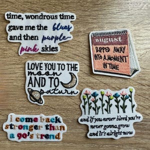 May include: A collection of embroidered patches with various phrases and designs. One patch reads "time, wondrous time gave me the blues and then purple pink skies." Another says "LOVE YOU TO THE moon AND TO saturn." Other patches include a calendar and floral designs.