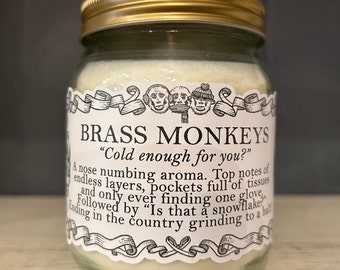 May include: A glass jar candle with a gold lid. The label reads "BRASS MONKEYS" and includes the text "Cold enough for you?" and other text. The candle has a creamy white wax.