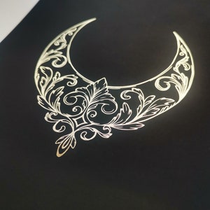 Pu&ograve; includere: Una mezzaluna dorata con intricati disegni floreali su uno sfondo nero.