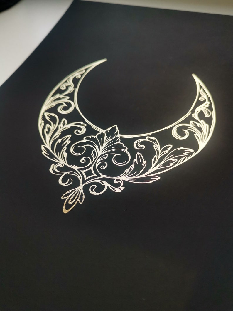 Pu&ograve; includere: Una mezzaluna dorata con intricati disegni floreali su uno sfondo nero.