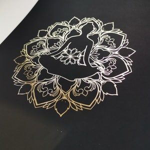 May include: A gold metallic silhouette of a person sitting in a lotus position, surrounded by a detailed mandala design on a black background.