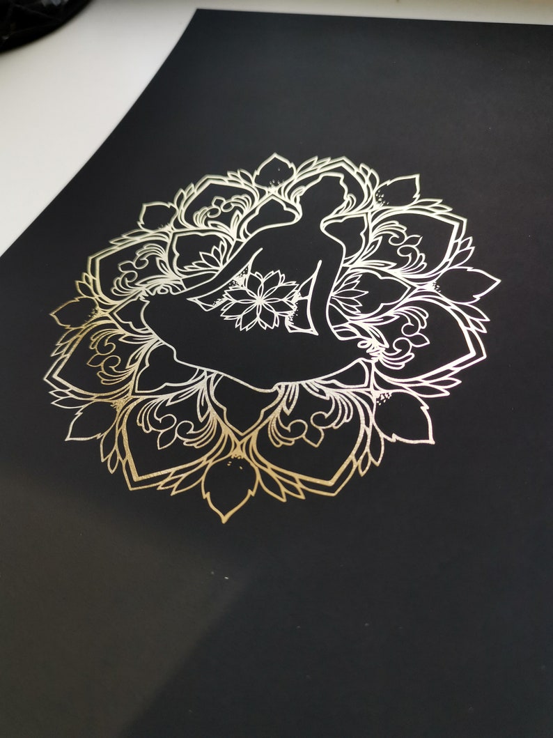 May include: A gold metallic silhouette of a person sitting in a lotus position, surrounded by a detailed mandala design on a black background.