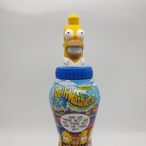 May include: A novelty water bottle with a yellow Homer Simpson head as the bottle cap. The bottle has a blue, red, and yellow design with the words "Belly Washers" and "The Simpsons" printed on it. The bottle also has the text "Are we there yet?" printed on it.