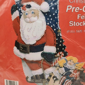 May include: A Christmas stocking kit with a felt Santa Claus design. The Santa has a white beard, red suit, and black belt. The stocking has a blue background with white polka dots and the name "Elaine" at the top.
