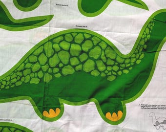 May include: A white fabric panel featuring a printed green dinosaur pattern with a textured scale design on the back, yellow feet, and black eye details. The fabric includes printed text labels like Dinosaur Side B and assembly instructions.