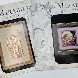 May include: Two cross-stitch patterns from Mirabilia, featuring a woman in a flowing gown and a woman with a moon and stars. Both patterns are framed in black and gold.