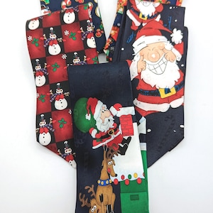 May include: A collection of four neckties featuring Christmas themes. One tie displays snowmen on a red and black checkered background, another shows Santa Claus, and a third depicts Santa with a reindeer. The fourth tie features reindeer patterns.