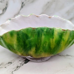 Könnte beinhalten: Eine Keramikschale mit gewelltem Rand, die eine lebendige grün-gelbe Außenseite aufweist. Der Innenraum ist ein weiches Weiß, was einen starken Kontrast erzeugt. Die Schale dient wahrscheinlich zum Servieren oder Ausstellen.
