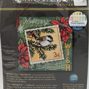 Puede incluir: Un kit de punto de cruz contado que presenta una escena navideña de invierno con un pájaro y la palabra "Wish" en una pancarta. El kit incluye hilo de algodón preordenado, tela Aida de marfil de 18 puntos, fieltro, aguja e instrucciones. El kit mide 11 cm de alto.
