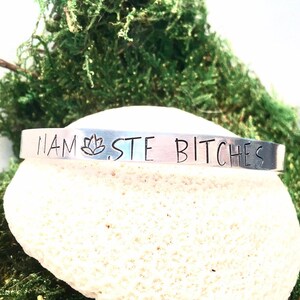 May include: Silver bracelet with the phrase "Namaste Bitches" and a lotus flower symbol engraved on it.
