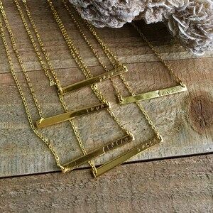 May include: Five gold bar necklaces with different words engraved on them. The words are "love", "be", "force", "sassy", and "together".