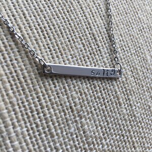May include: A silver necklace with a thin bar pendant that says "salty".