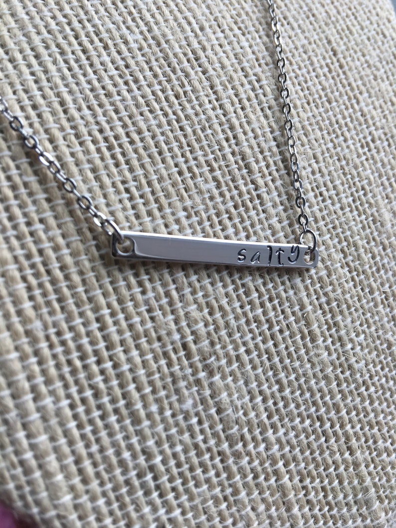 May include: A silver necklace with a thin bar pendant that says "salty".