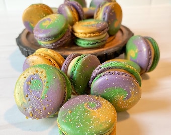 May include: A close-up of a group of colorful macarons with green, purple, and gold swirls. The macarons are arranged on a wooden surface.
