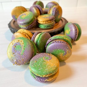 May include: A close-up of a group of colorful macarons with green, purple, and gold swirls. The macarons are arranged on a wooden surface.