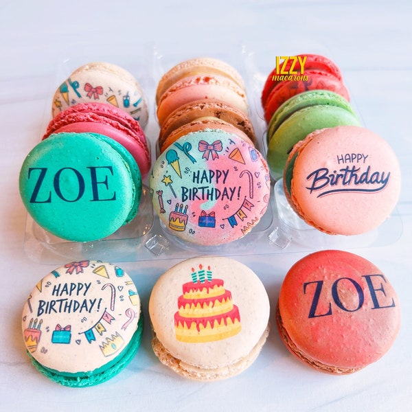 Könnte beinhalten: Eine Auswahl bunter Macarons in einer durchsichtigen Kunststoffschale. Einige tragen den Namen ZOE, andere den Schriftzug HAPPY BIRTHDAY und einer zeigt eine dreistöckige Torte. Der Markenname IZZY macarons ist in der oberen rechten Ecke zu sehen.