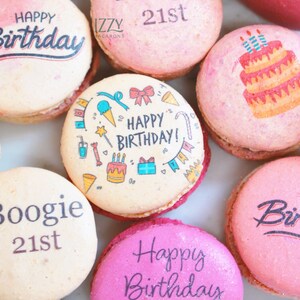 May include: A collection of colorful macarons with various designs and text. Some macarons have "Happy Birthday" or "Boogie 21st" printed on them. Other macarons feature illustrations of a cake, ice cream, and gifts. The macarons are pink, white, and red.