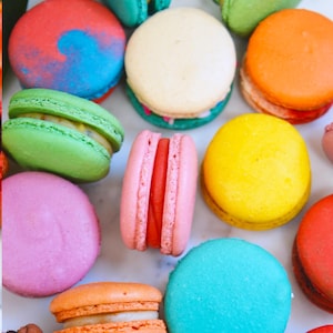 May include: An assortment of colorful macarons in various shades, including pink, green, yellow, orange, blue, and red. The French pastries are arranged closely together, showcasing their round shape and filling. The image highlights the vibrant colors and textures of the sweet treats.
