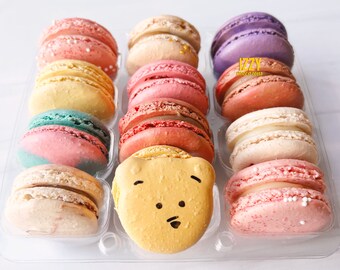 May include: A box of 12 colorful macarons, including a yellow macaron with a bear face. The macarons are arranged in a clear plastic container. The box is labeled "IZZY macarons".